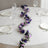 Floral table runner with purple and pink flowers on a white table setting.
