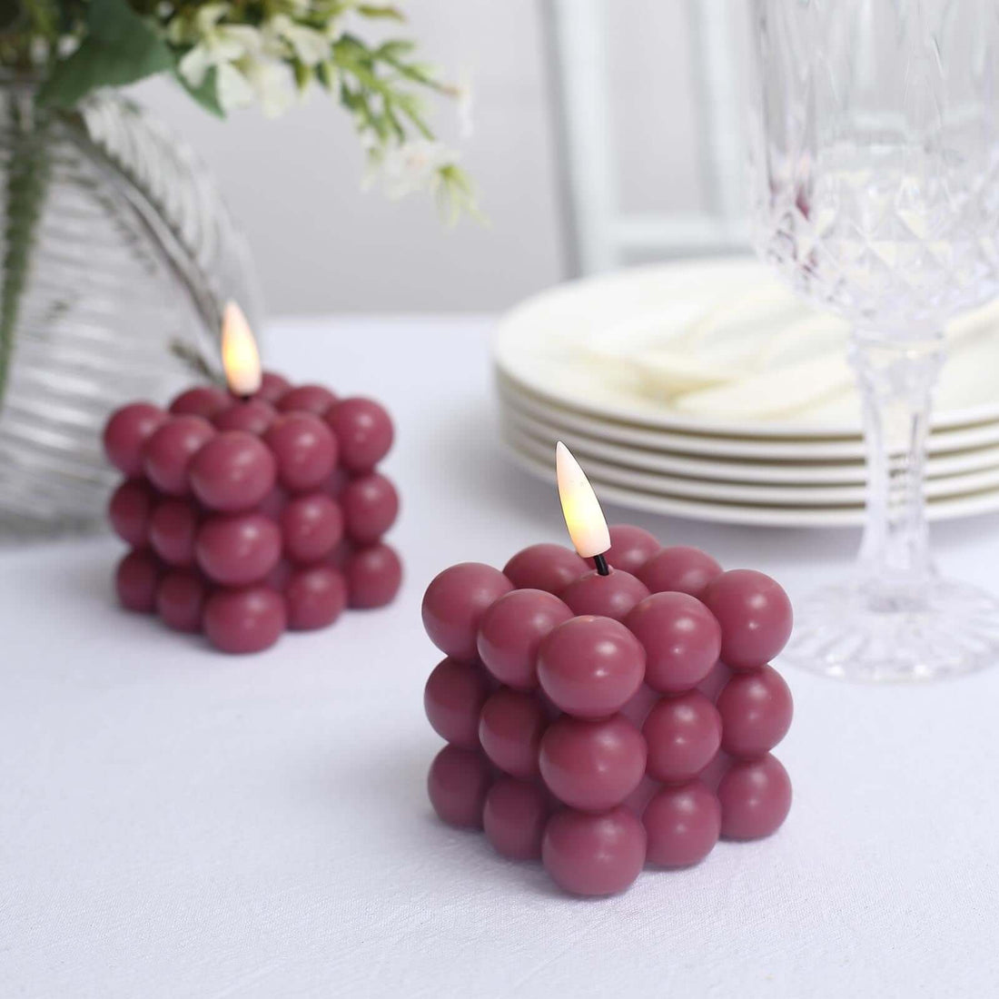 Purple bubble candle design with lit wick, set on a table with dining ware.