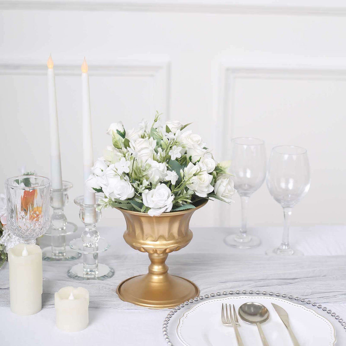 Gold vase with white flowers on a dining table setting.