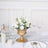 Gold vase with white flowers on a dining table setting.