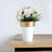 White pot with gold band holding artificial flowers on a wooden table.