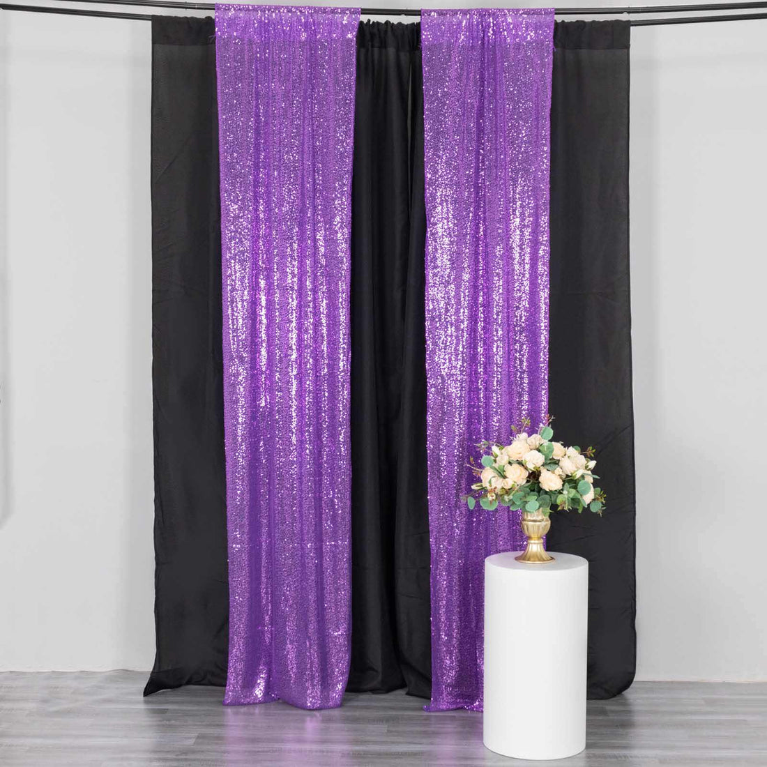 Purple sequin backdrop with black curtain and floral arrangement on a pedestal.