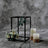 Black metal lantern with faux flowers and candles on textured gray backdrop.