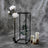Decorative black lantern with peonies and candles on a textured backdrop.