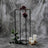 Black metal flower stand with purple flowers and candles on a textured gray background.