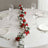 Floral table runner with red and white flowers on a dining table setting.