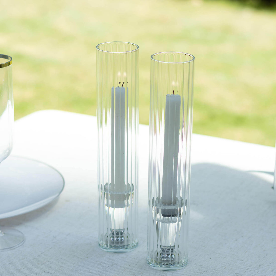 Two elegant glass candle holders with white candles inside.