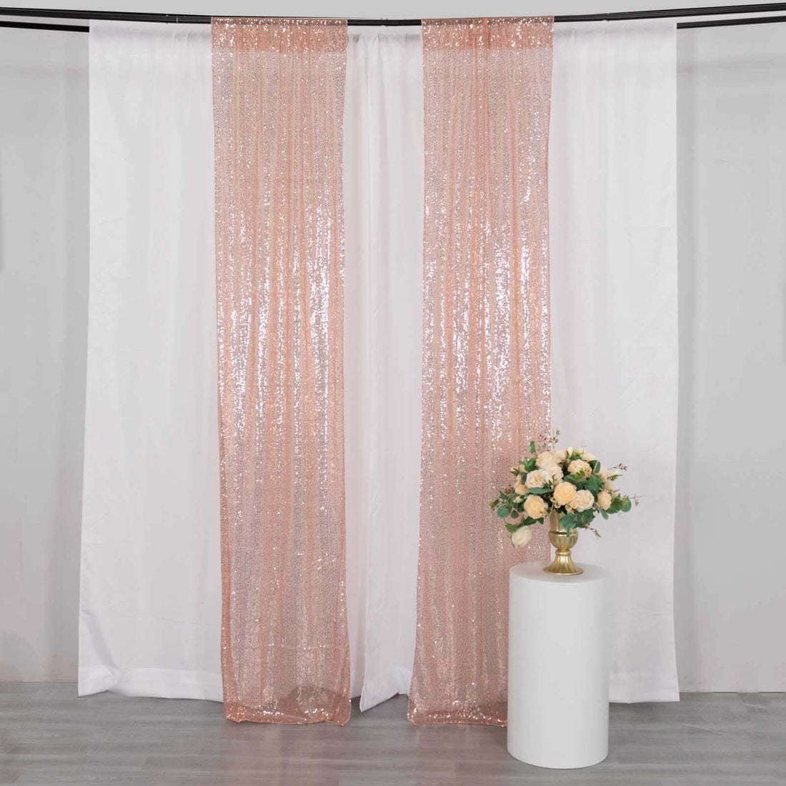 Rose gold sequin curtains draped with a floral arrangement on a pedestal.