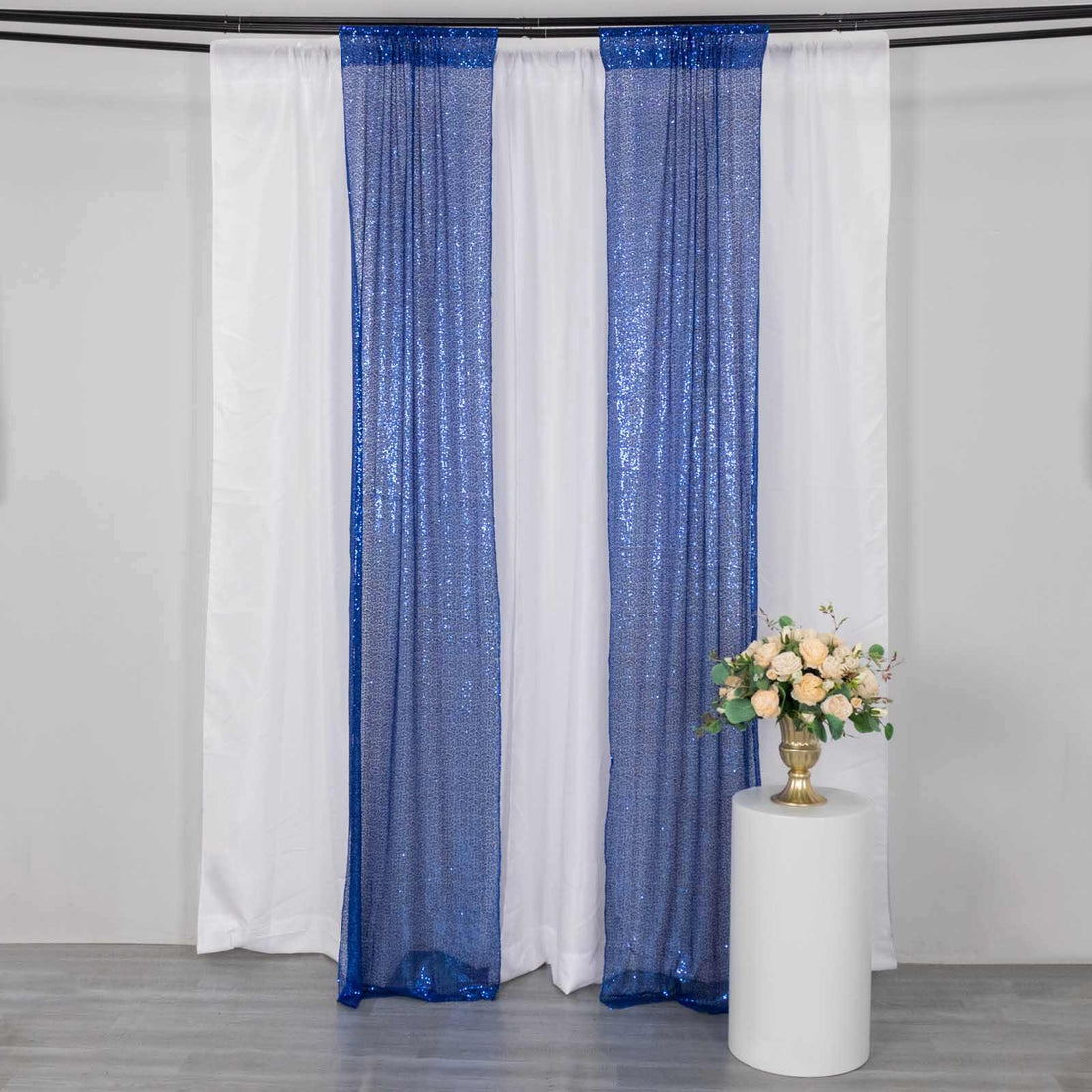 Blue sequin curtain drapes on a white backdrop with a floral arrangement.