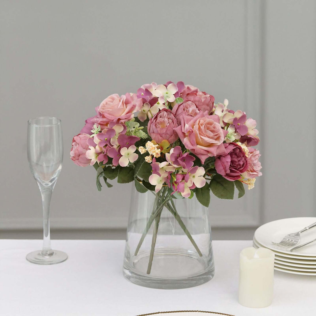 Floral arrangement with pink roses and mixed flowers in a clear glass vase.