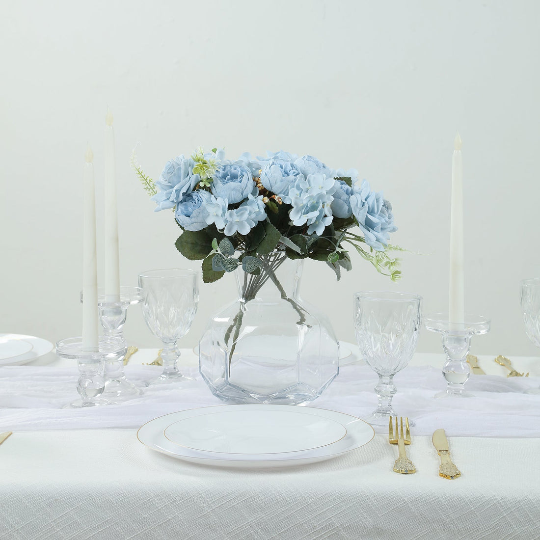 Blue floral centerpiece with candles and dinnerware on a dining table.
