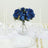 Blue floral centerpiece in a glass vase on a table setting with white plates and candles.