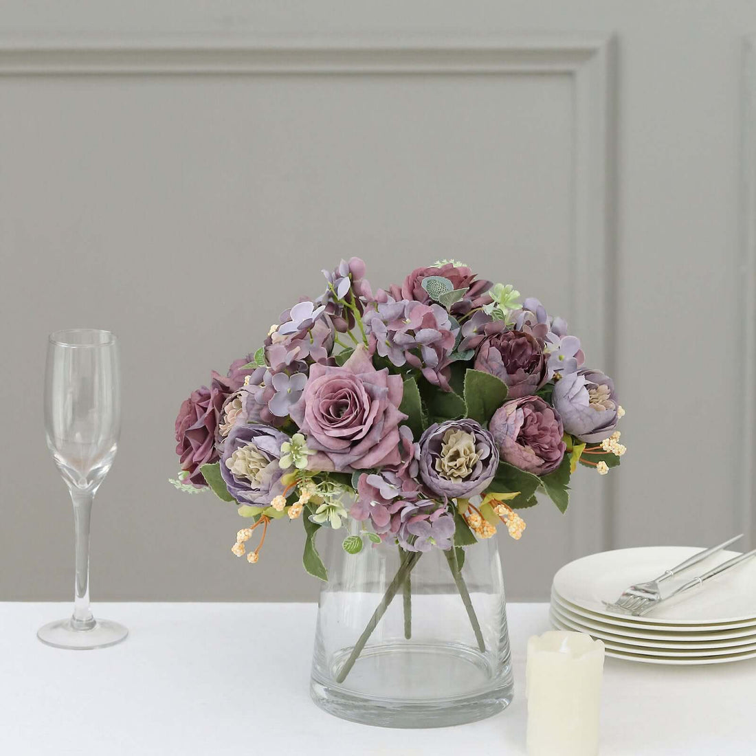Purple floral arrangement in a glass vase with elegant table setting.