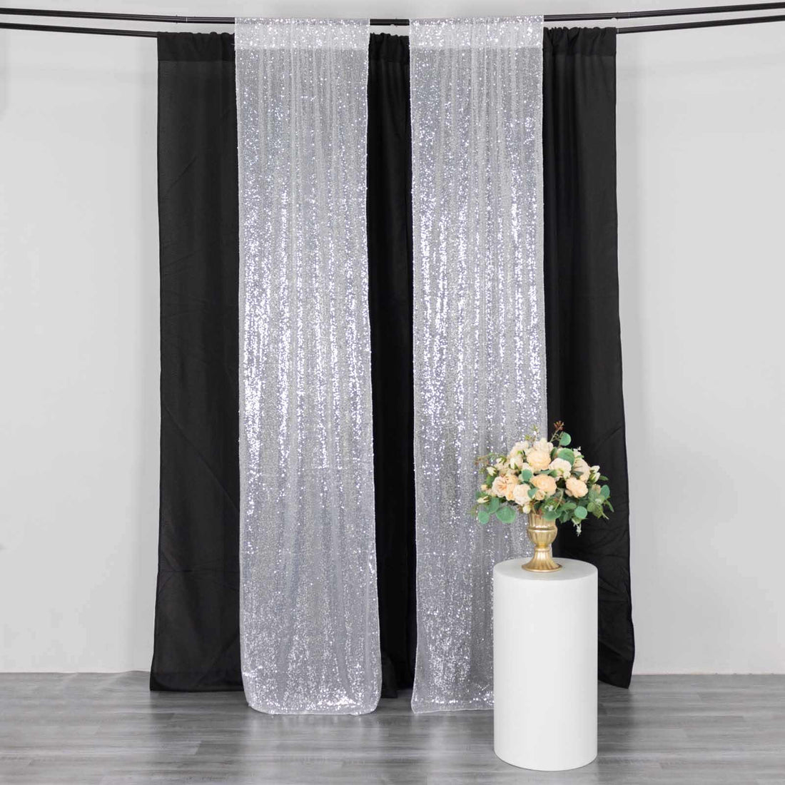 Sparkling silver curtains with black backdrop and floral arrangement on a pedestal.