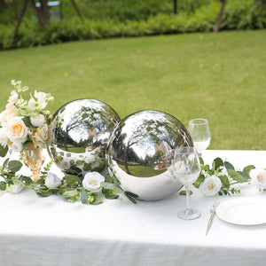 Decorative silver spheres on a table with flowers and glassware in a garden setting.