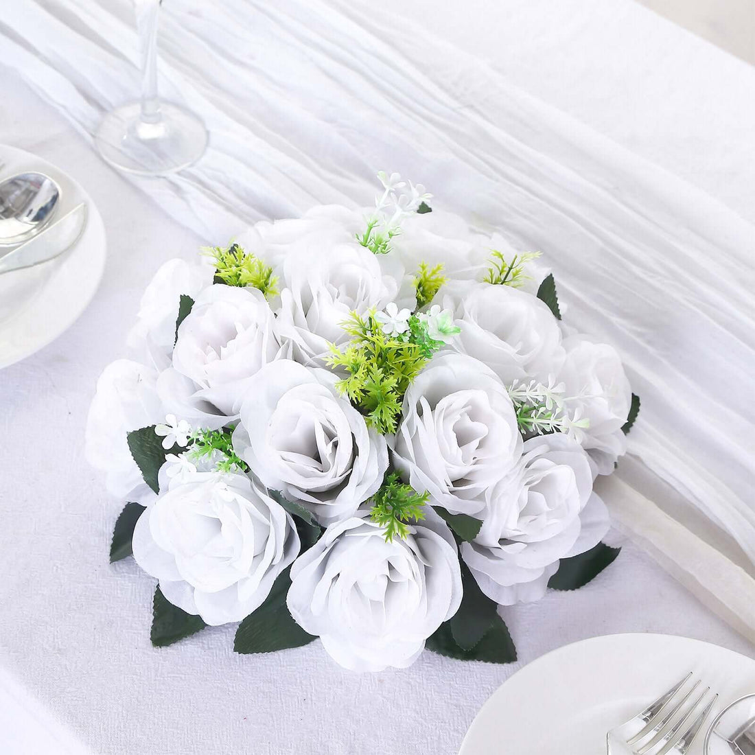 White artificial rose bouquet with green accents on a table setting.