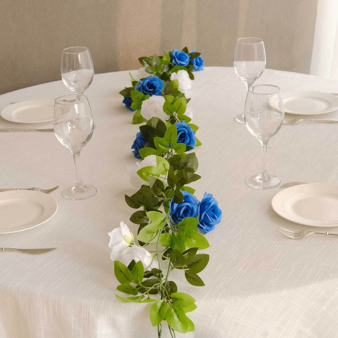 Elegant table setting with blue and white rose garland and glassware.