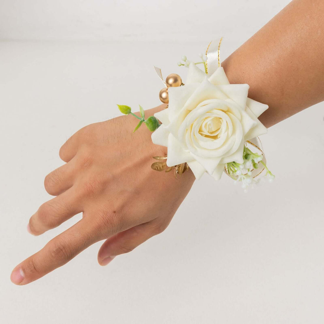White rose wrist corsage with greenery and decorative accents.