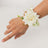White rose wrist corsage with greenery and decorative accents.
