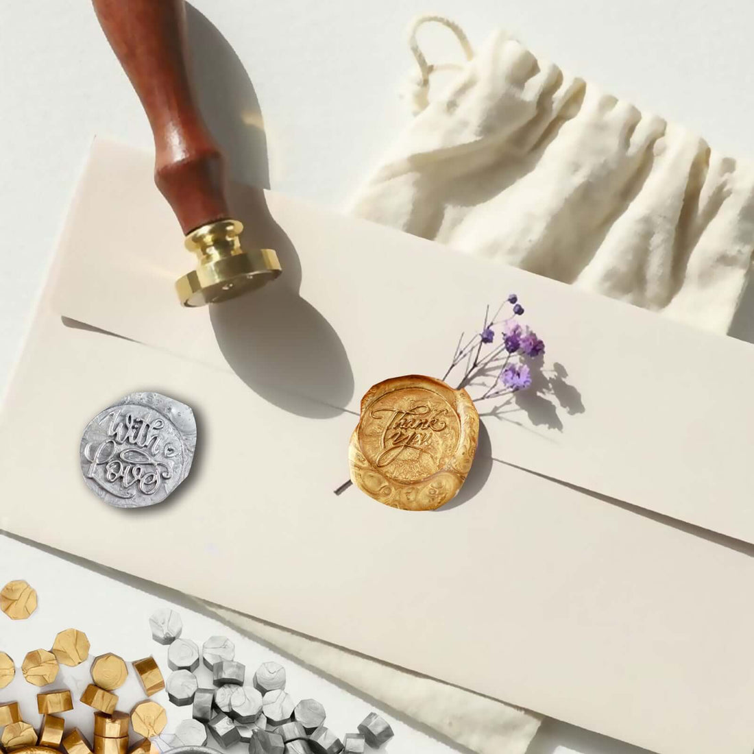 Wax seal stamp set with gold and silver seals on an envelope with dried flowers.