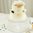 Elegant white cake adorned with roses and a gold crown on a clear cake stand.