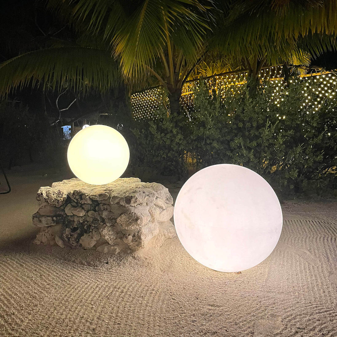 Two glowing decorative spheres on a stone pedestal in a tropical setting.