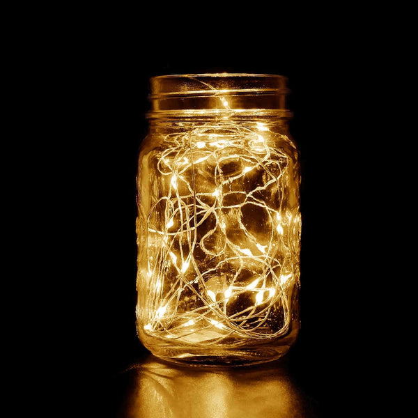Mason jar filled with warm white fairy lights glowing in the dark. #whtbkgd