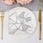Silver geometric napkin on elegant dinner plate with gold utensils.