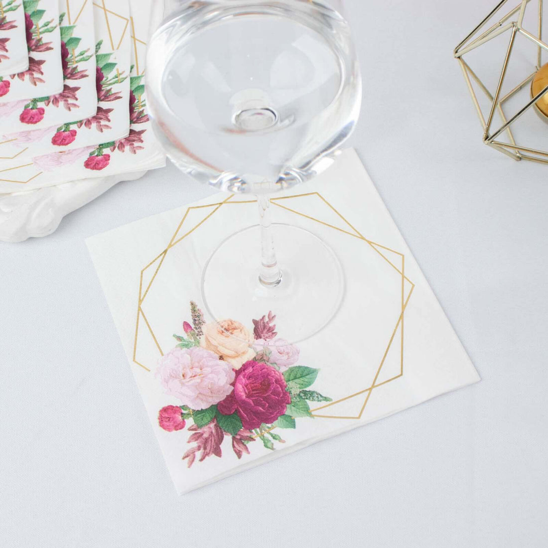 Floral decorative napkin with geometric gold accents and a glass on top.