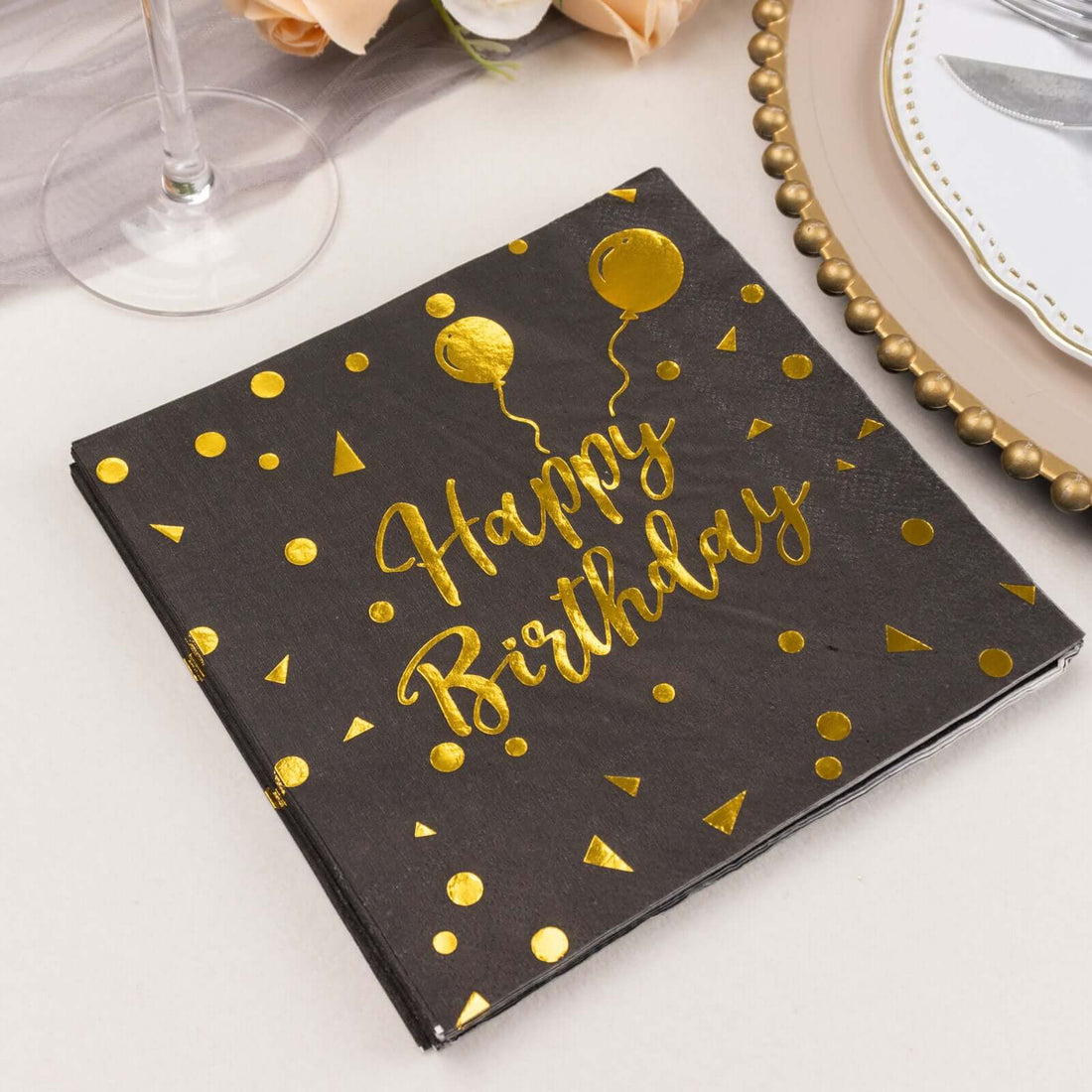 Black birthday napkin with gold "Happy Birthday" text and balloon design.