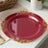 Elegant red plate with gold ornate rim design on a white background.