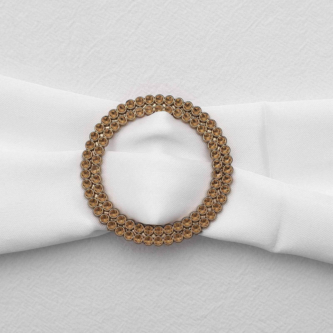 Gold circular napkin ring with crystal accents on a white napkin.
