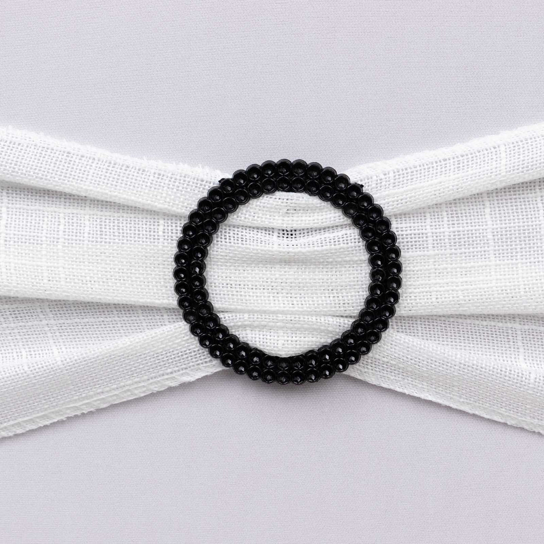 Black beaded oval hair accessory on white fabric backdrop.