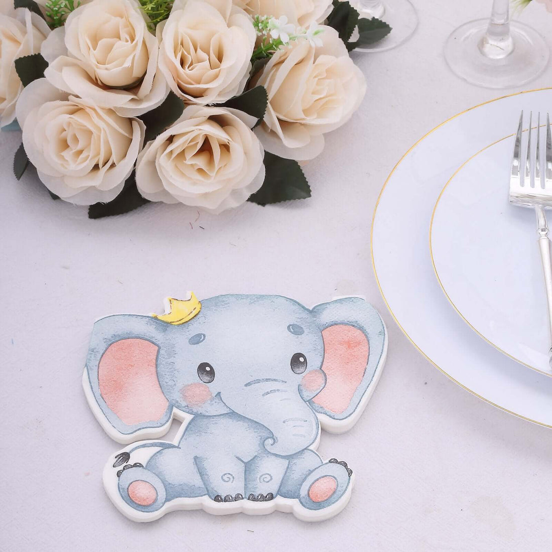 Cute elephant decoration with a crown, surrounded by roses and tableware.