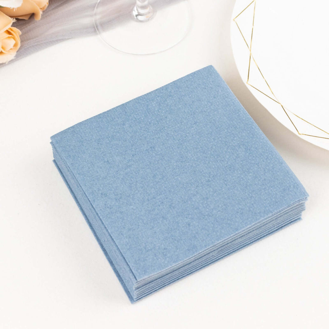 Blue cloth napkins stacked on a table beside a plate and wine glass.