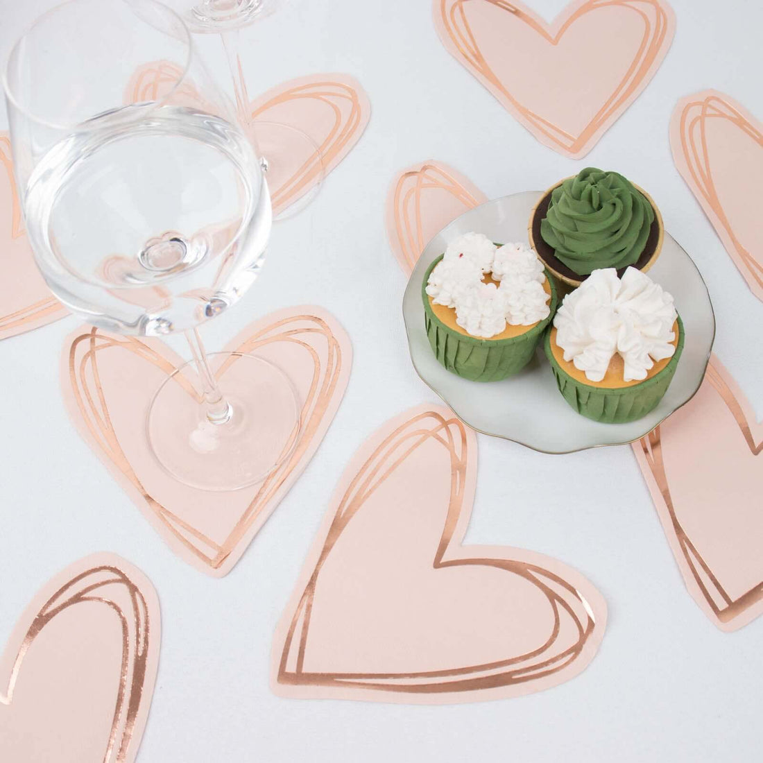 Heart-shaped dessert table with cupcakes and a glass of water.