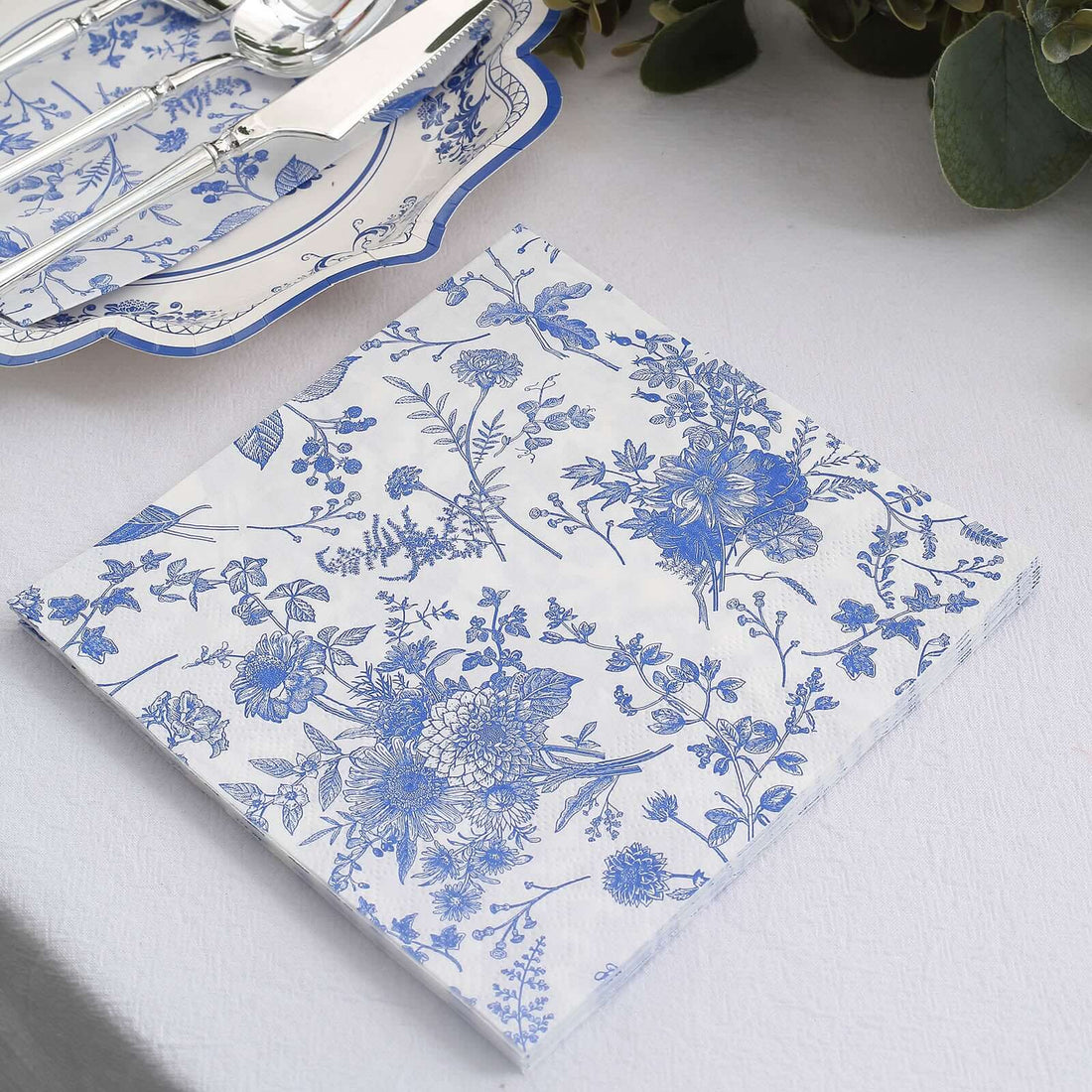 Blue floral paper napkin on a table setting with cutlery.