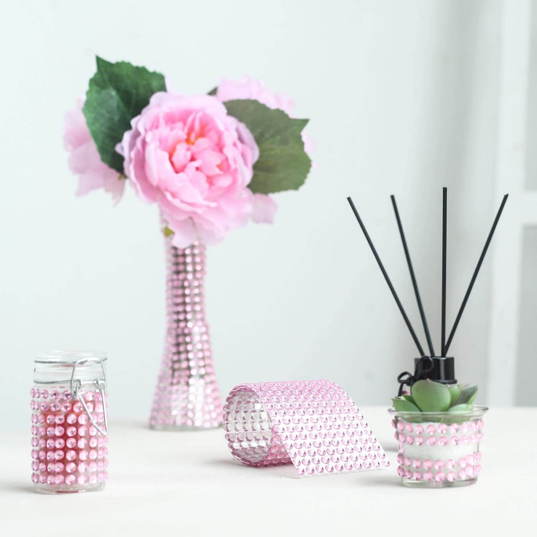 Decorative pink flower vase, candle holder, and ribbon on a table.