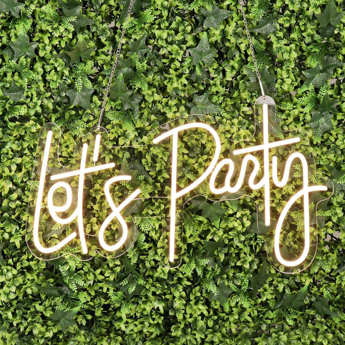 Neon "Let's Party" sign against a green foliage background.
