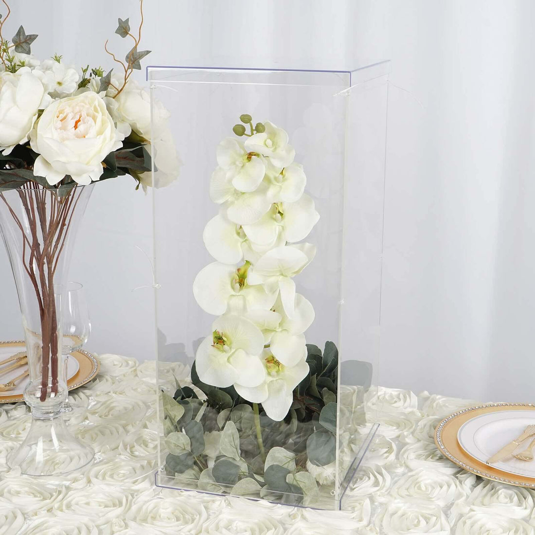 Orchid arrangement in a clear display case on a decorative table setting.
