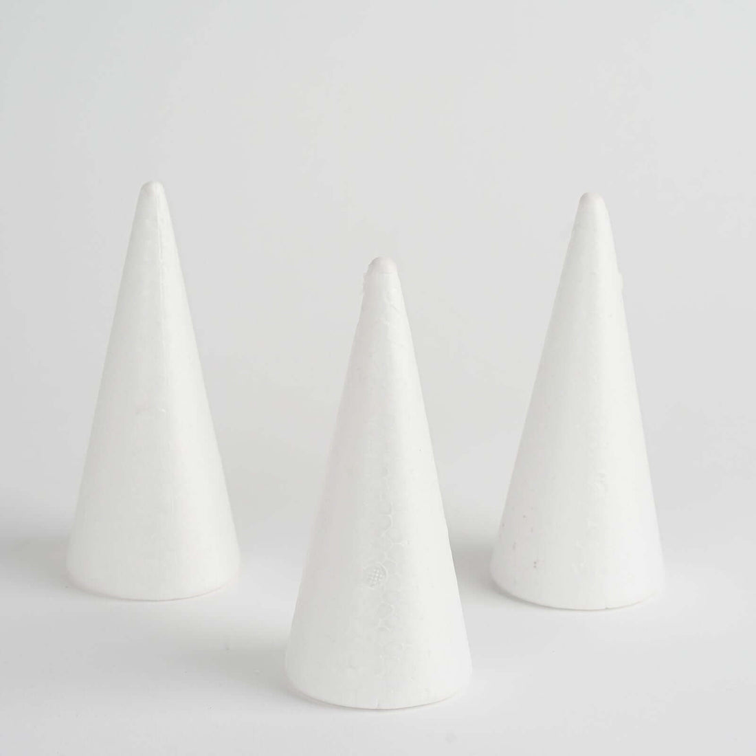 Three white conical crafting foam shapes on a plain background
