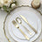 Elegant gold cutlery set on decorative white plates with floral arrangement.