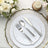 Elegant silver cutlery set on a white plate with gold trim, surrounded by floral decor.