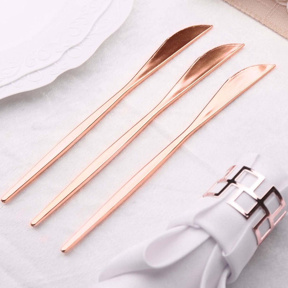 Set of three elegant rose gold butter knives on a soft white tablecloth.