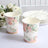 Floral paper cups on a table with white plates and flowers in the background.