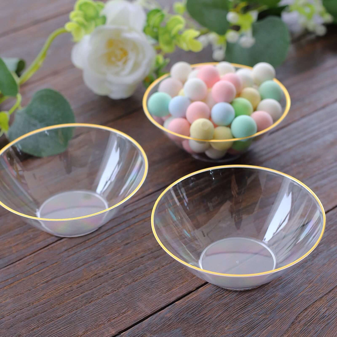 Clear plastic bowls with gold trim and pastel candy on a wooden surface.