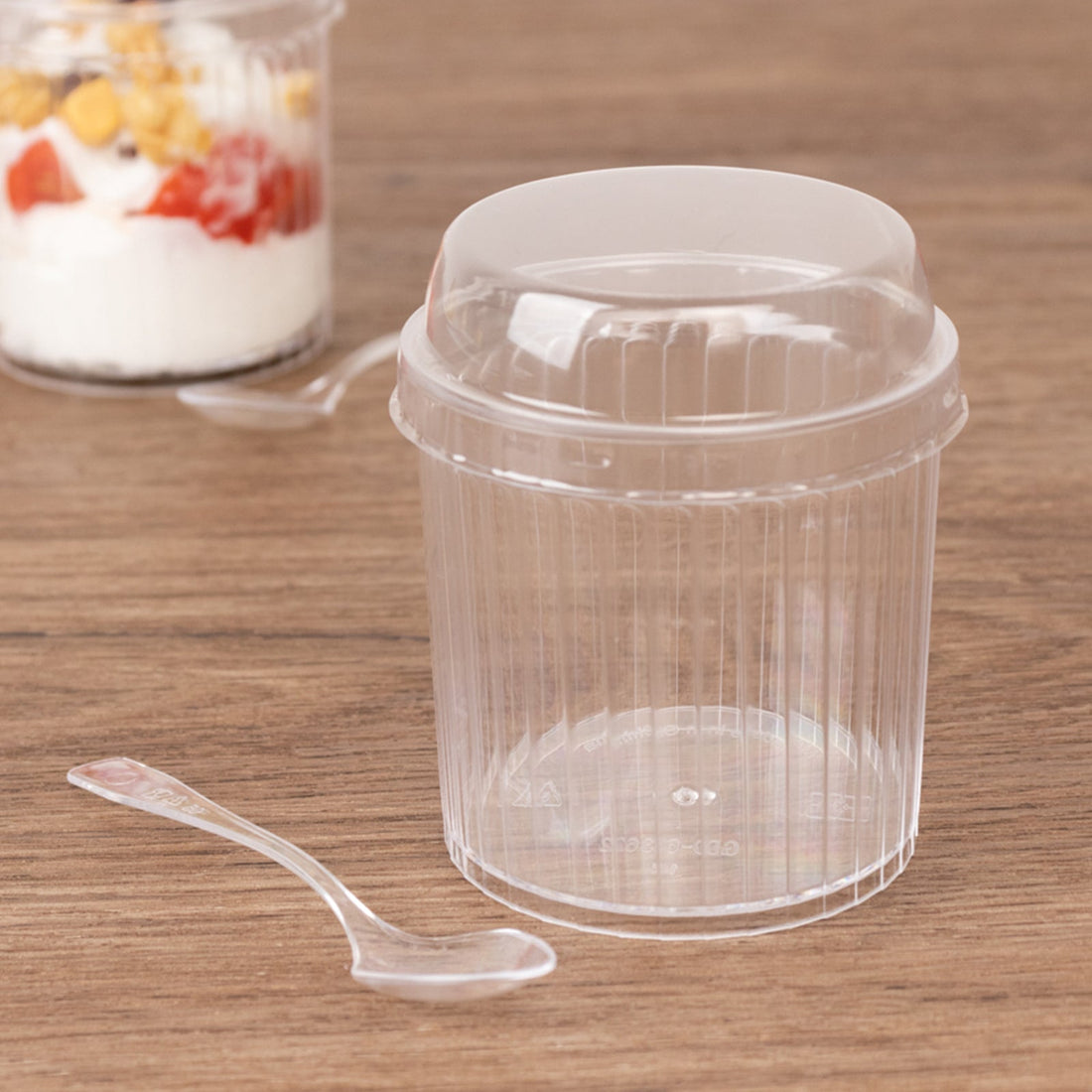 Clear plastic cup with lid and spoon on wooden surface.