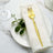 Gold fork on a white napkin and plate, with greenery accent.