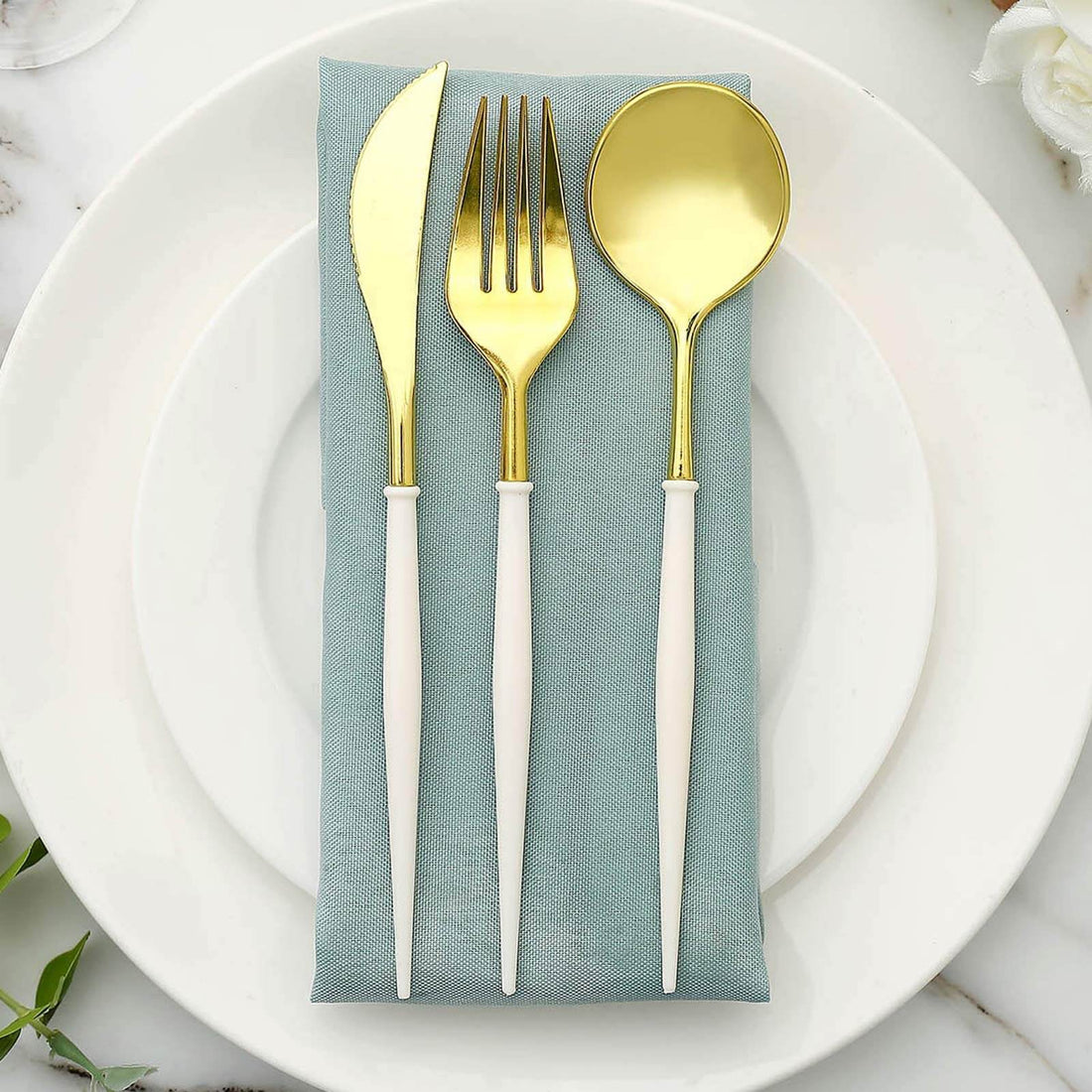 Gold cutlery set on a light blue napkin atop a white plate.