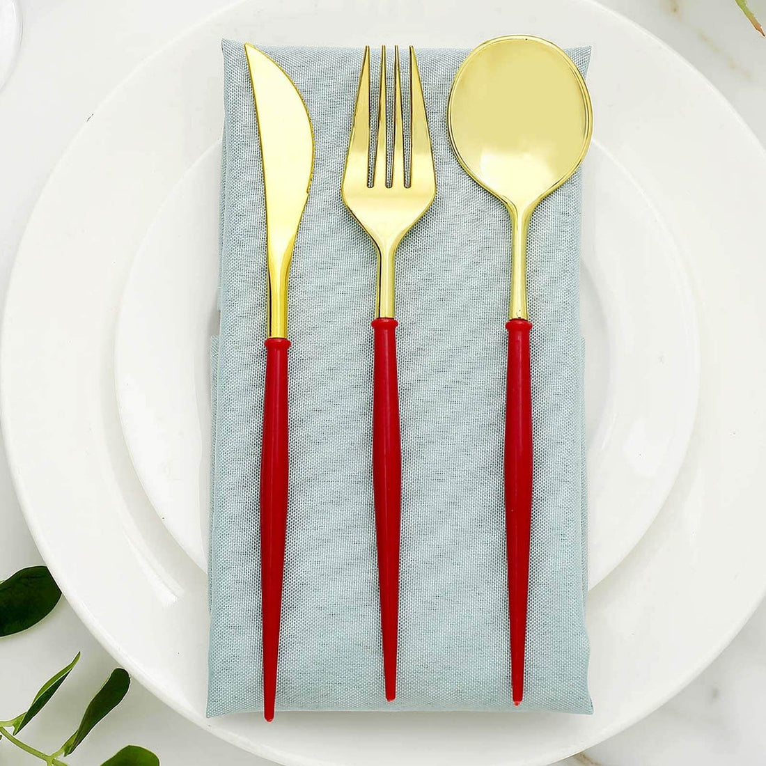 Gold cutlery set with red handles on a blue napkin atop a white plate.